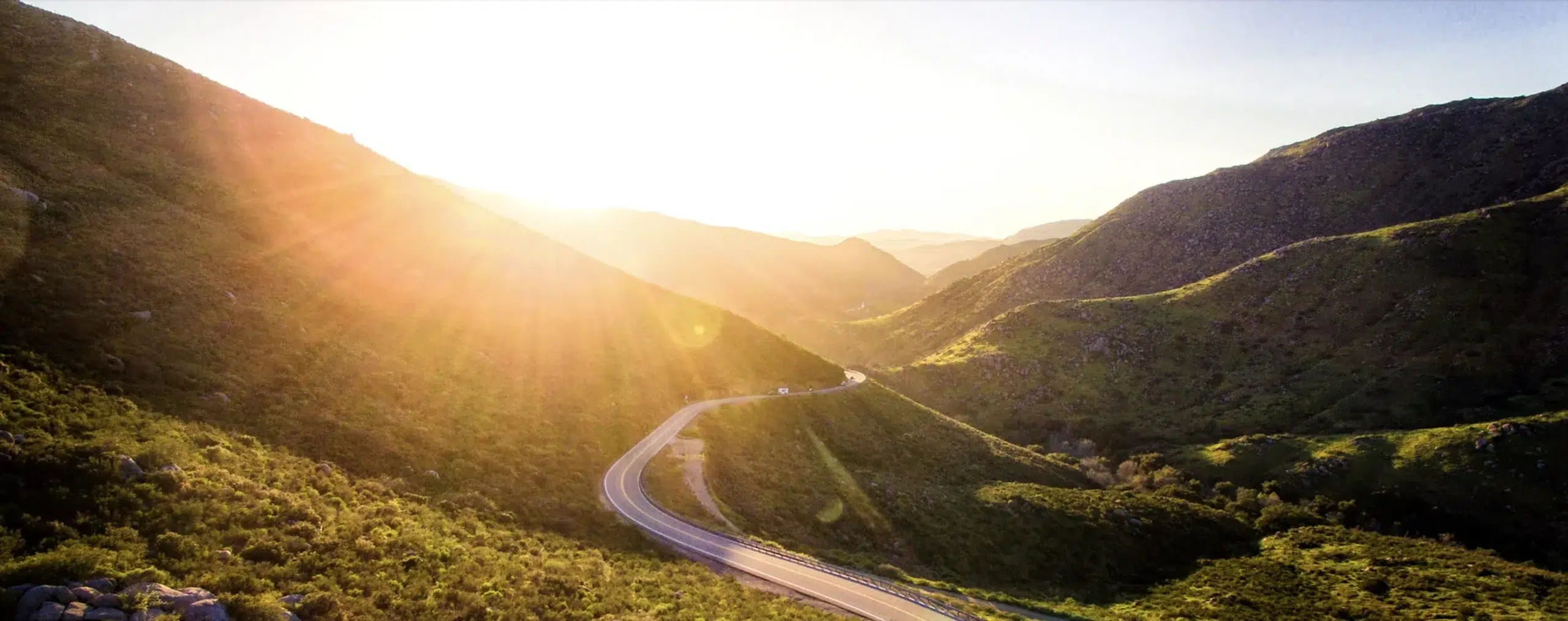Sun rising over rolling green hills giving them a golden glow.