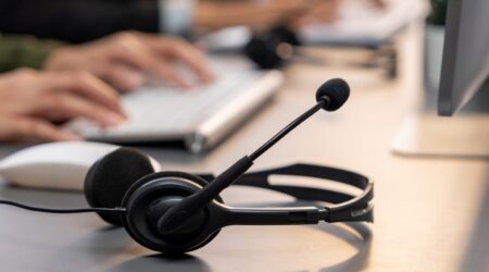 Close-up of headset on a call center desk with blurred customer support agent in background.