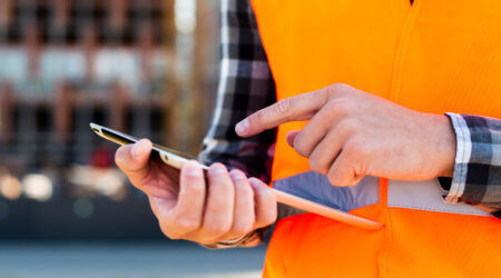 A person wearing a safety vest is holding a smartphone and pointing at the screen.
