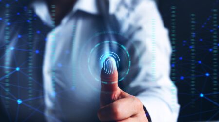 A person in a button-up shirt is pressing their thumb on a fingerprint scanner, with digital elements in the background.
