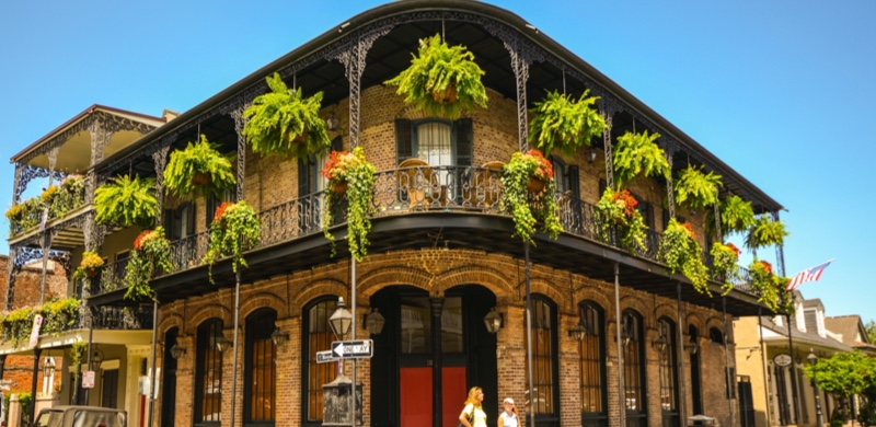 Historic building with wrought iron balconies and hanging plants on a street corner under a clear blue sky.