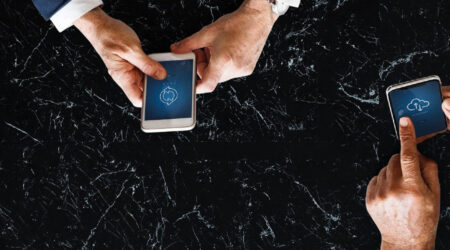 Two sets of hands holding smart phones over a black marble table.