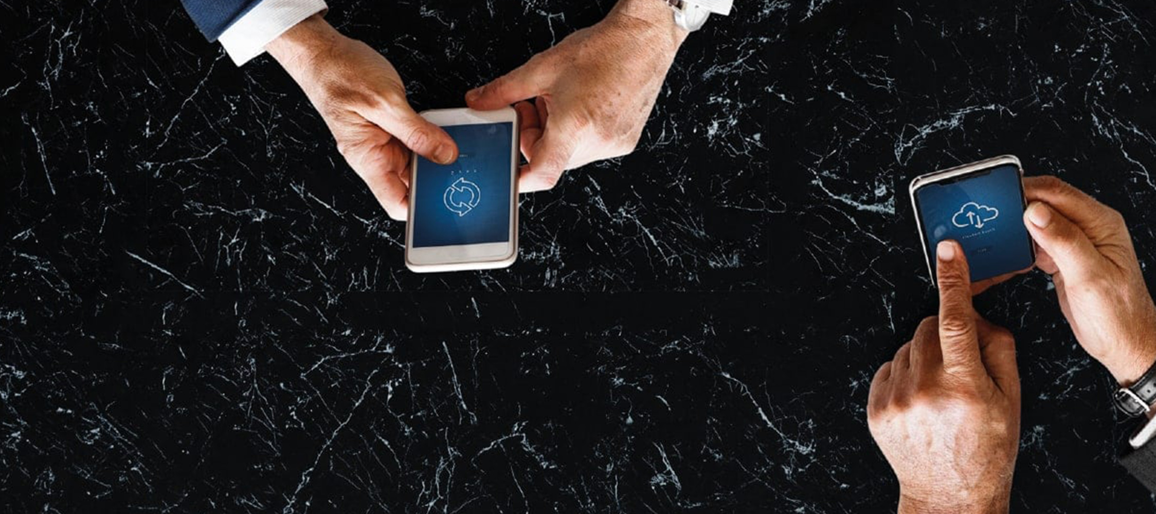 Two sets of hands holding smart phones over a black marble table.