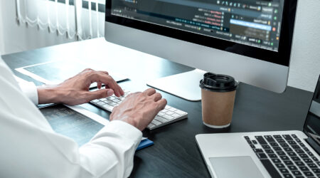 person typing on computer with coffee and technical content on monitor.
