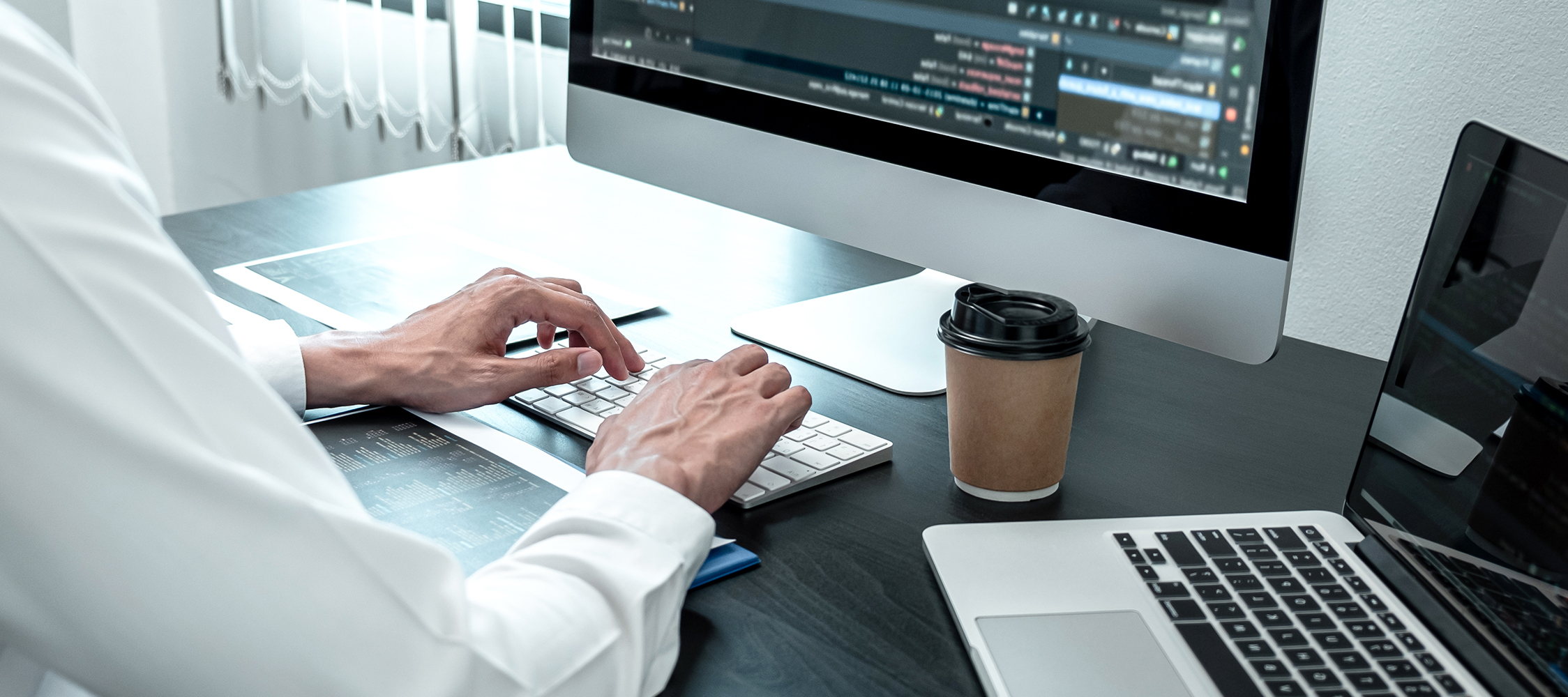 person typing on computer with coffee and technical content on monitor.