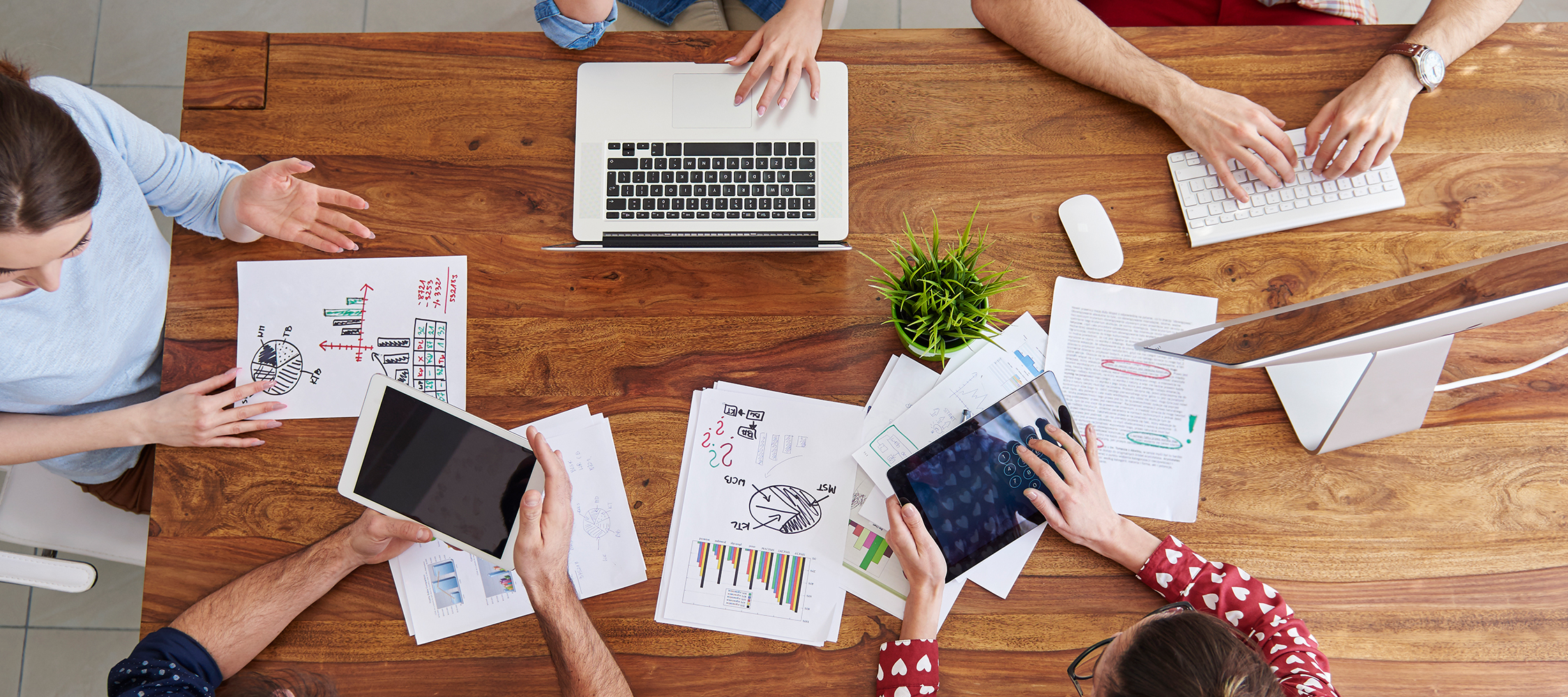 People around table in office with laptops, tablets, and data projections.