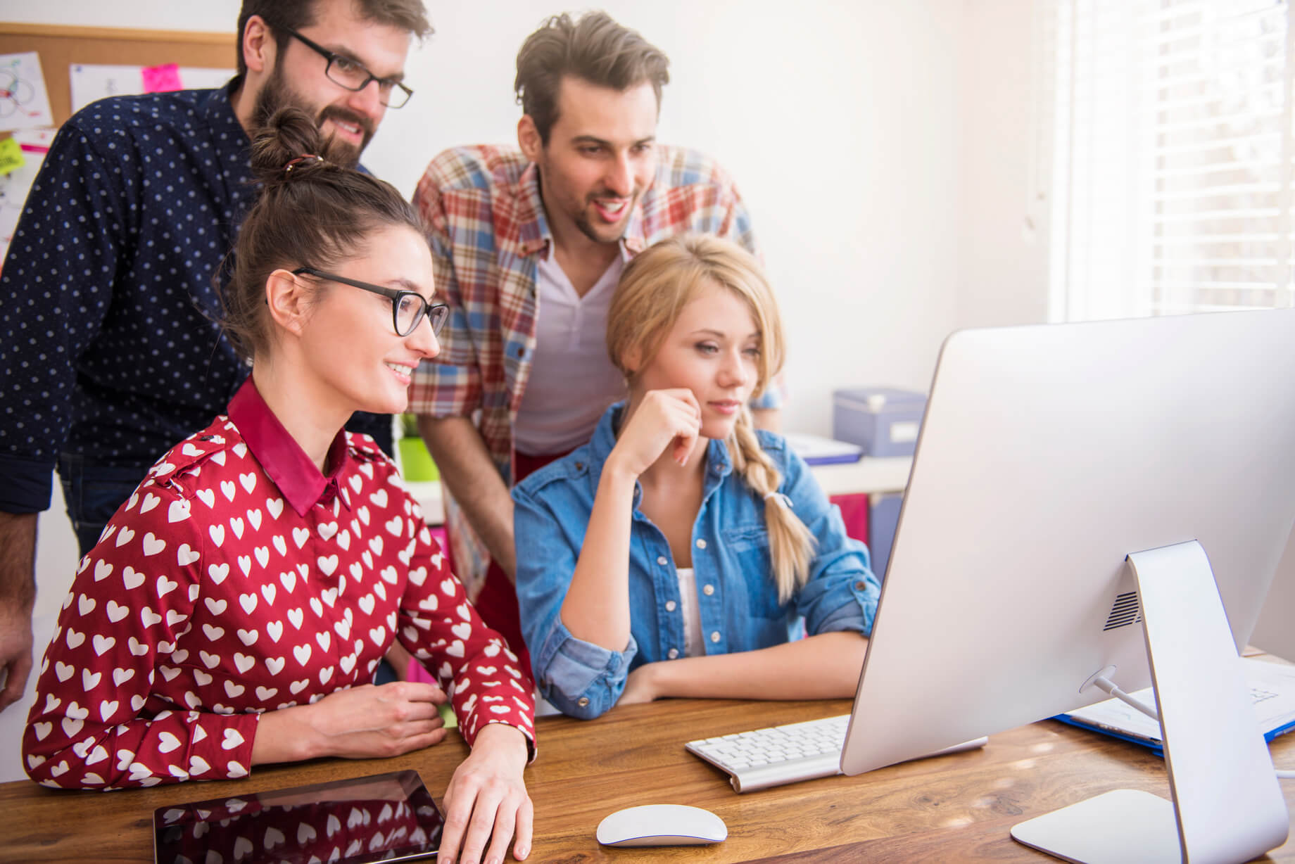 Group of coworkers gathered around a computer, collaborating for some task in a bright modern office.
