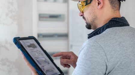 On site technician wearing protective gear and using tablet to look at technical diagrams.