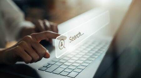 Close-up of a hand pressing a digital search bar on a laptop screen representing online browsing.