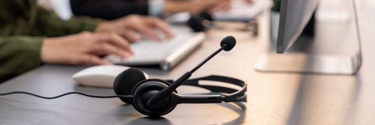 Close-up of headset on a call center desk with blurred customer support agent in background.