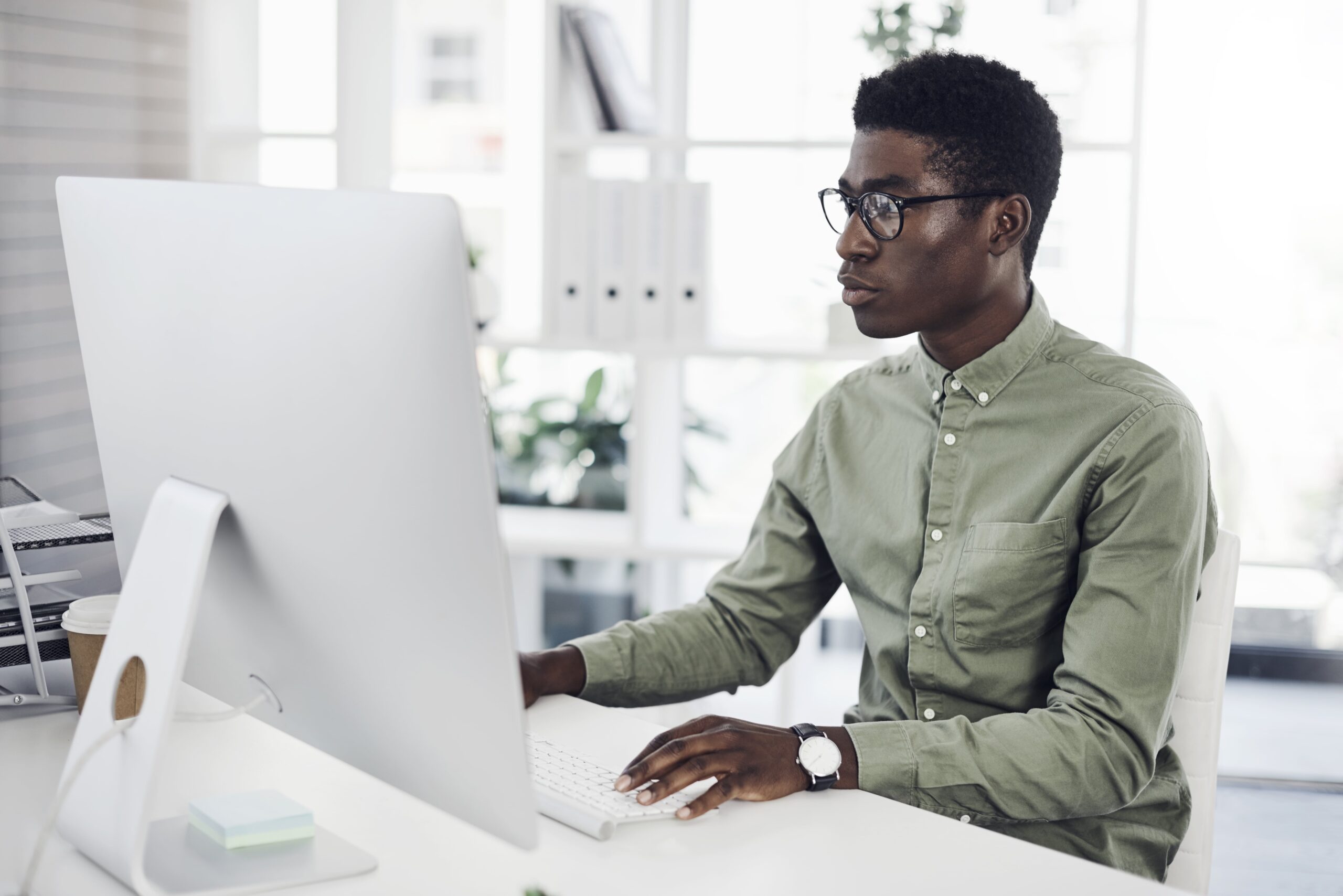 Man typing on computer in office with large desktop screen.
