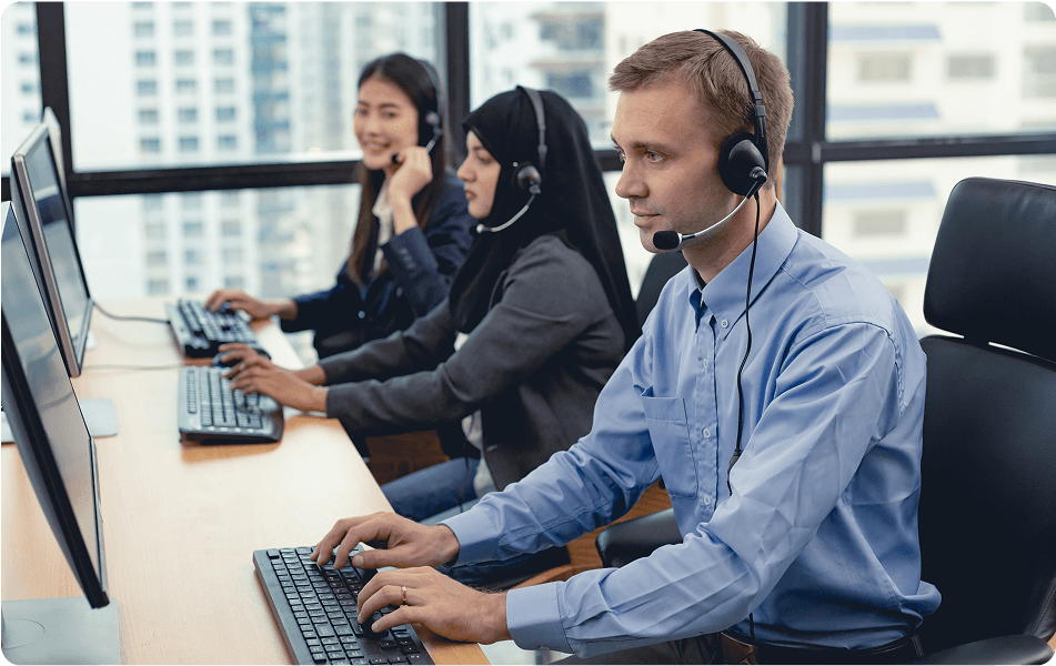 Three call center employees working at desks with computers in a modern office setting.
