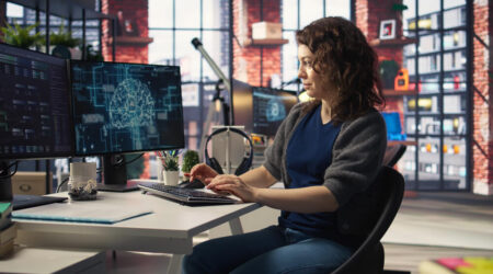 Woman in an office, typing, and looking at computer monitors that show AI.