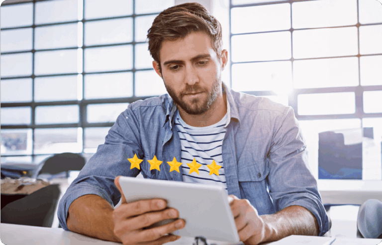 A man sits at a table in a bright room, looking at a tablet. Five yellow stars indicating a top rating appear in front of the tablet screen.
