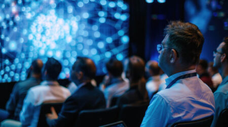 Group of people sitting and watching presentation on large screen in conference room.