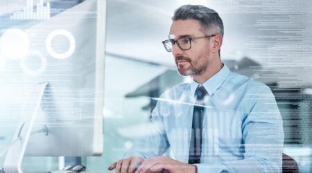 Man in a tie and button down shirt on a desktop computer with code and graphs digitally overlaid.
