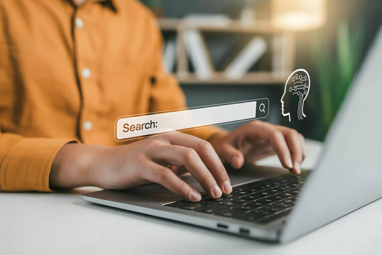 A person sitting at a desk, using a laptop with a holographic search bar and AI icon in the middle of the image.