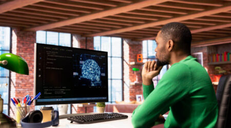 Man sitting at a desk looking at a computer screen that says AI.