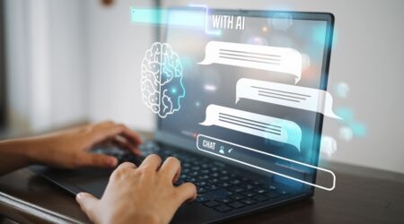 Person typing on a laptop with virtual chat bubbles and a brain icon representing artificial intelligence displayed above the keyboard.
