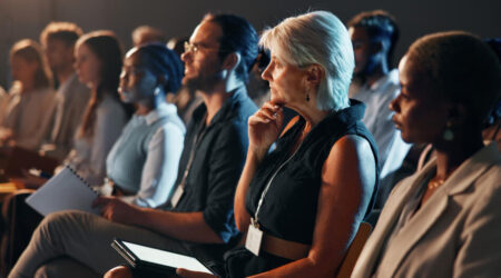 Side view of a row of people sitting, listening, and taking notes at a conference.