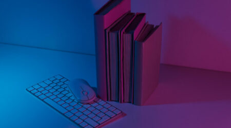 Books next to a keyboard and mouse with blue and pink lighting.