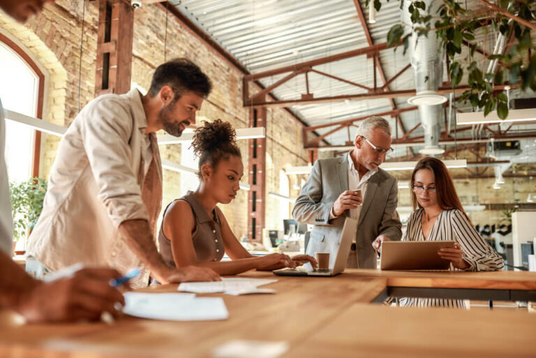 Colleagues standing around a table in an industrial workspace and looking at each others' laptops.