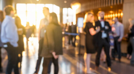 Business professionals mingling indoors with natural light from large windows.