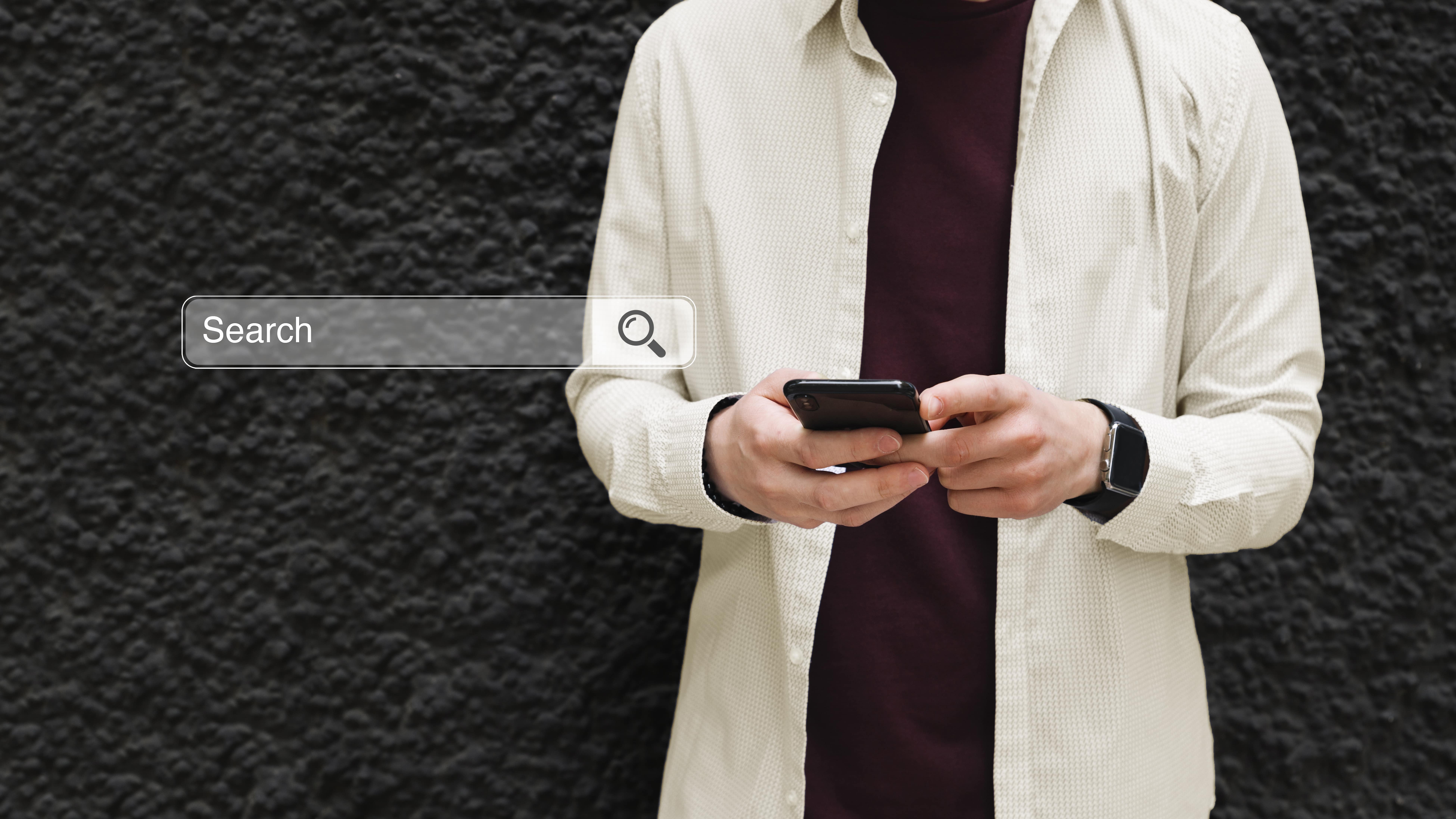 man against black wall holding phone with search bar.