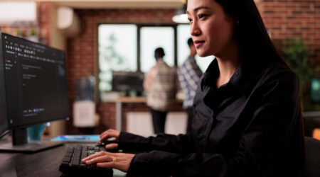 Woman coding software on desktop computer at office desk.