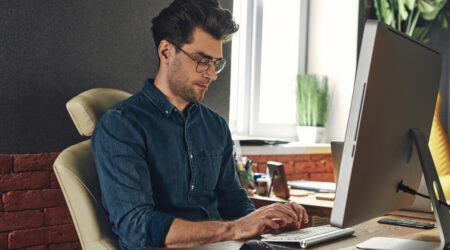 Man sitting at a desk and typing on the computer while looking down at his keyboard.