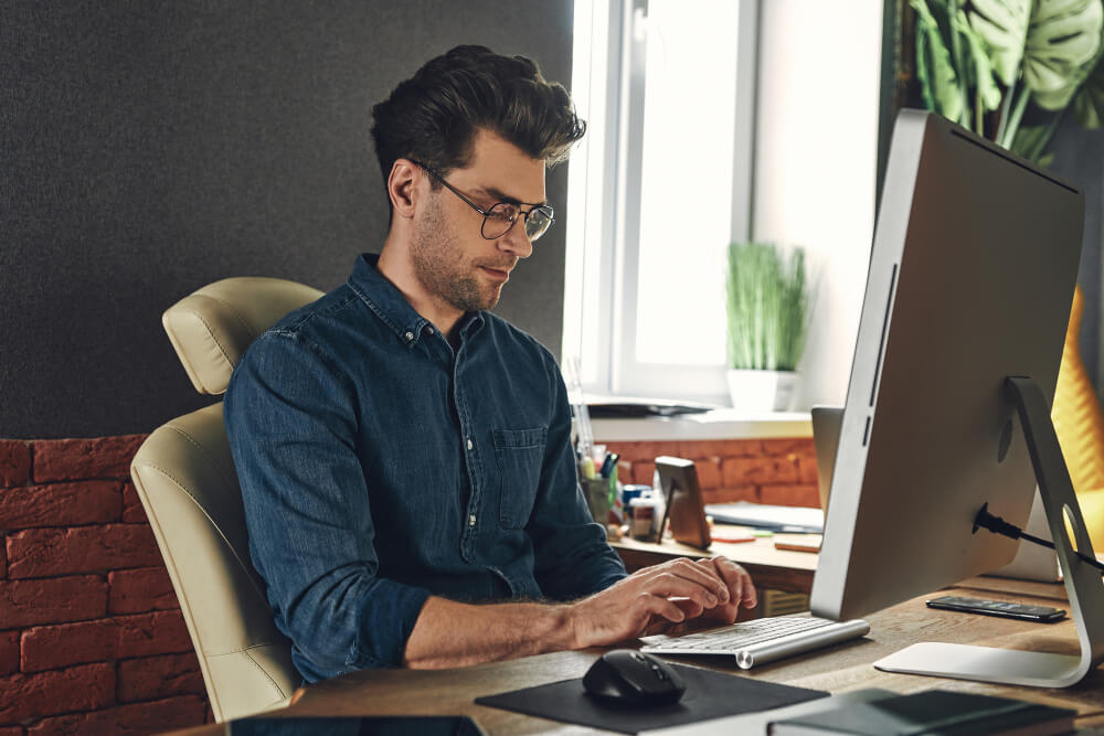 Man sitting at a desk and typing on the computer while looking down at his keyboard.